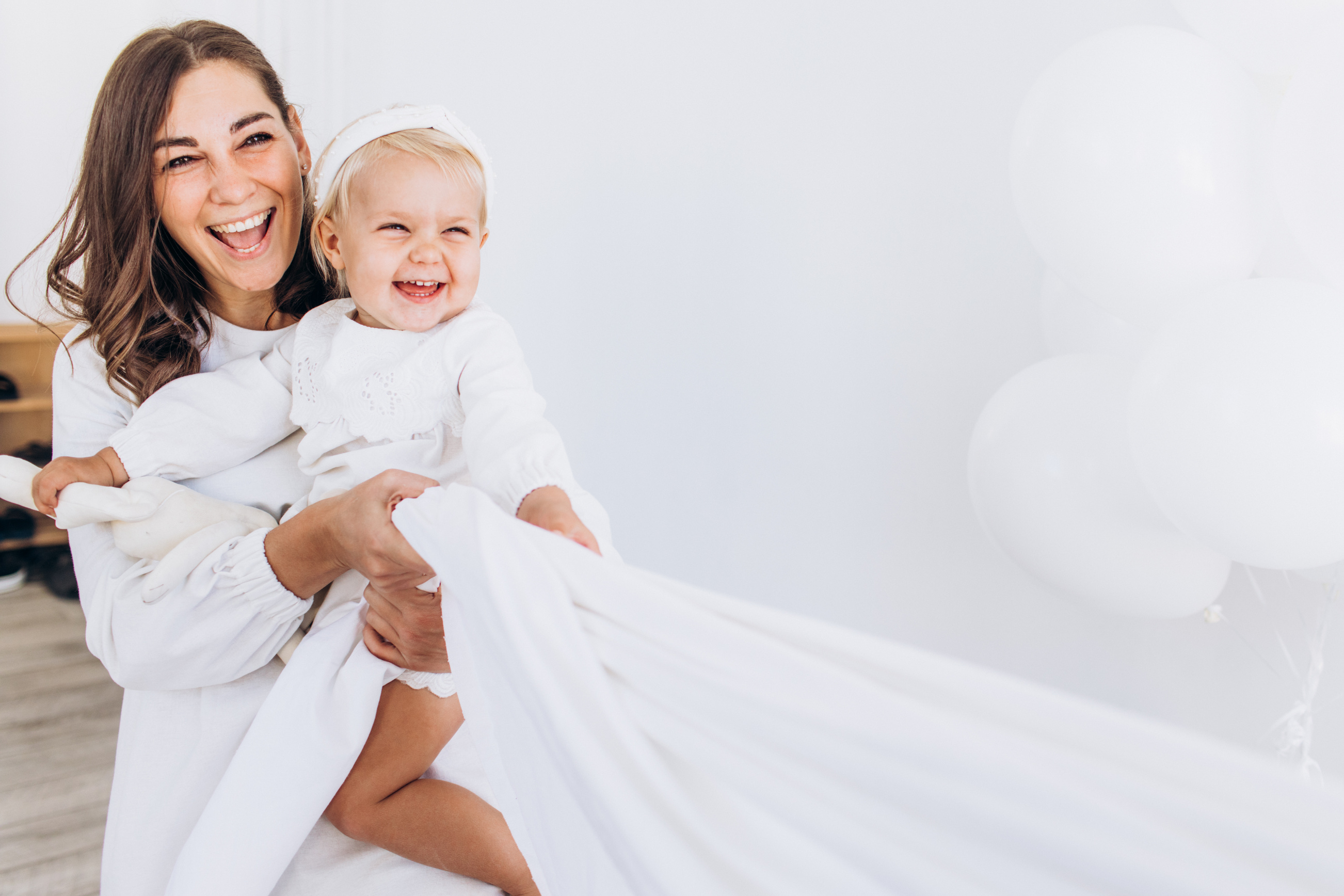 Mom and daughter play with a sheet. The baby and mom are smiling.